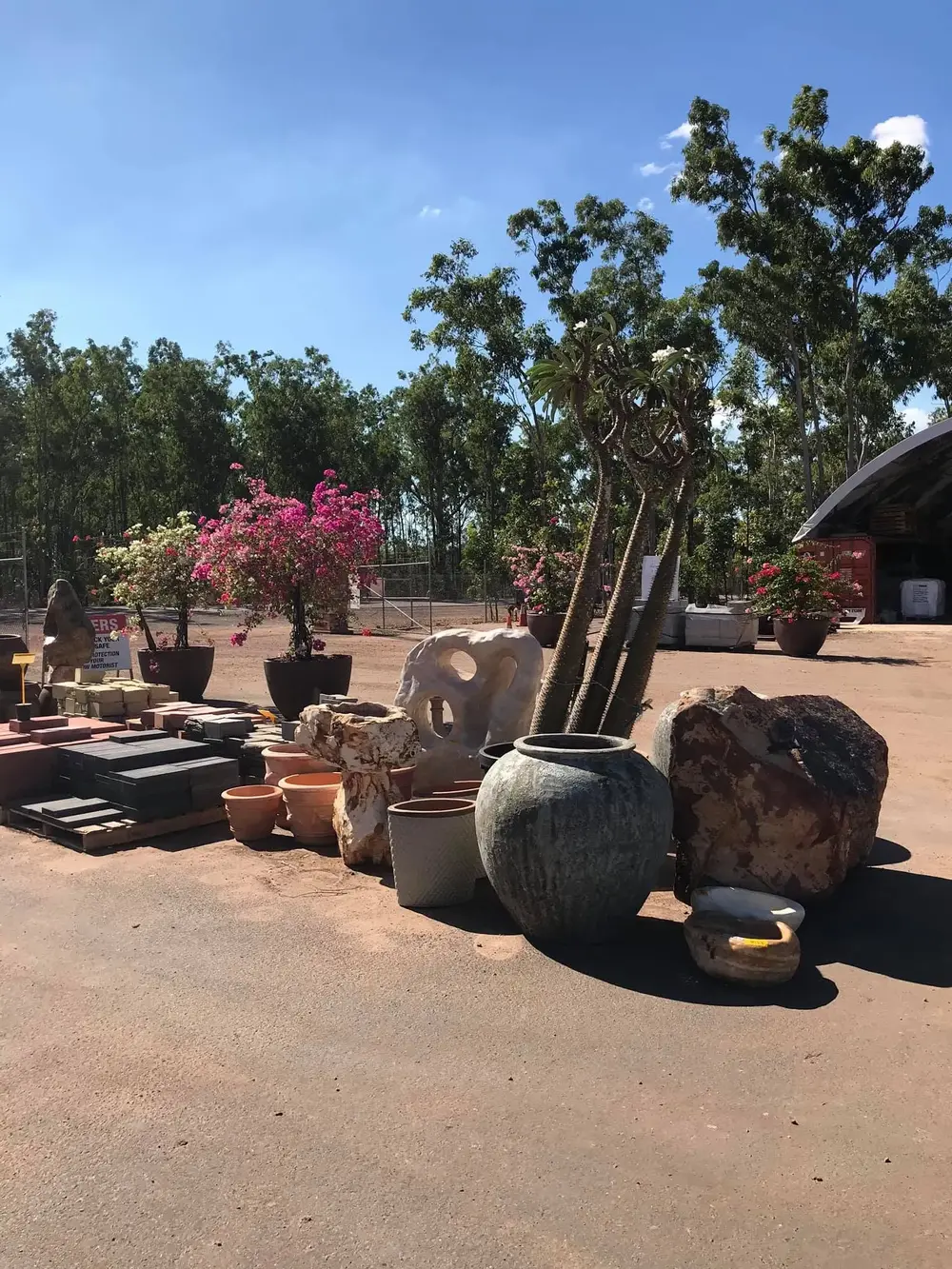 Outdoor stone and pot display framed by flowering plants